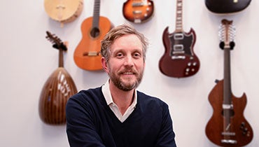 Georgetown University Music Program Professor Ben Harbert sits in his office, with a wall covered in different acoustic and electric guitars.